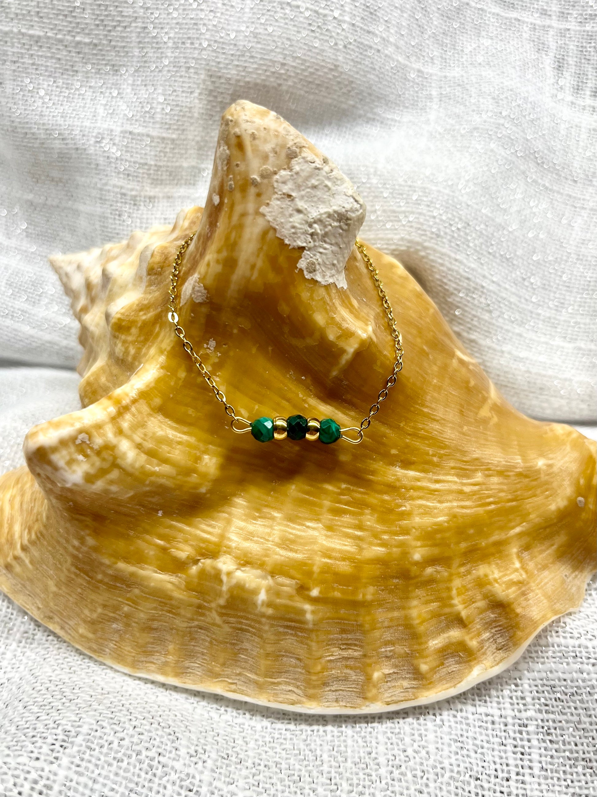 Bracelet MALIA, de couleur dorée avec pierres de Malachite, exposé sur un coquillage.