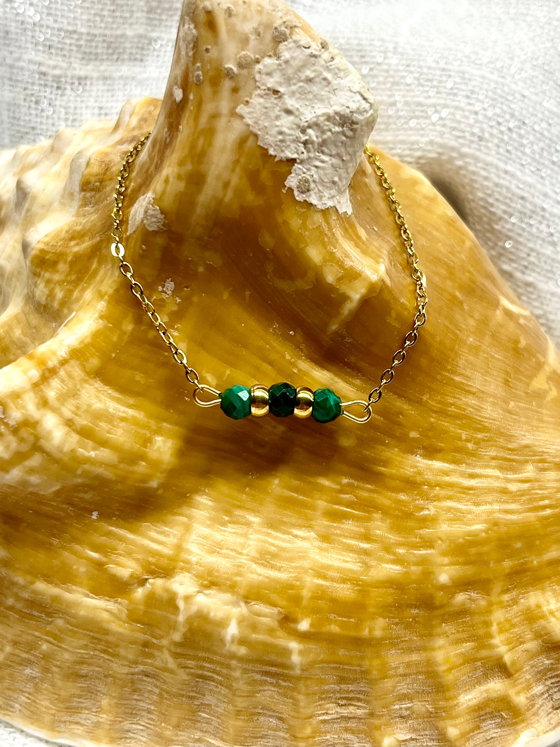 Bracelet MALIA, de couleur dorée avec pierres de Malachite, exposé sur un coquillage.