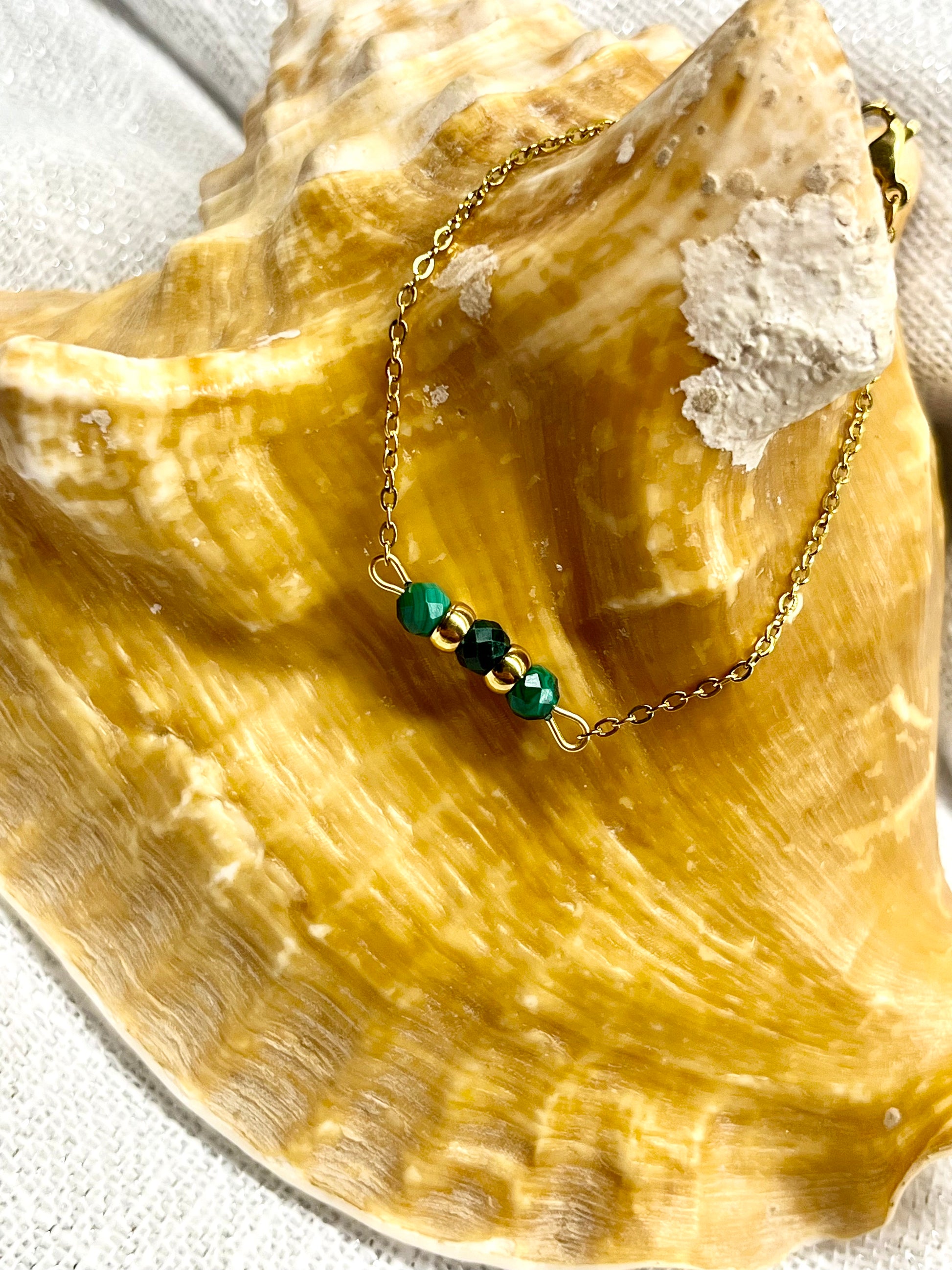 Bracelet MALIA, de couleur dorée avec pierres de Malachite, exposé sur un coquillage.