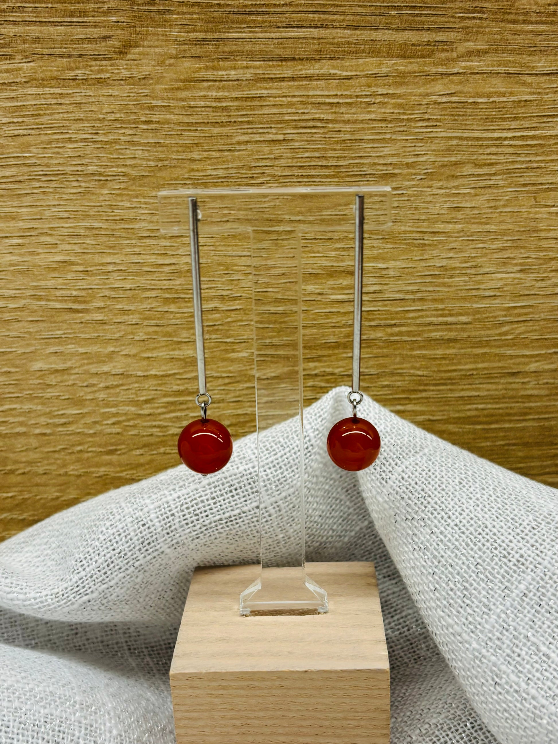 Boucles d'oreille MANON en pierre de Cornaline, exposées sur un fond en bois et lin.