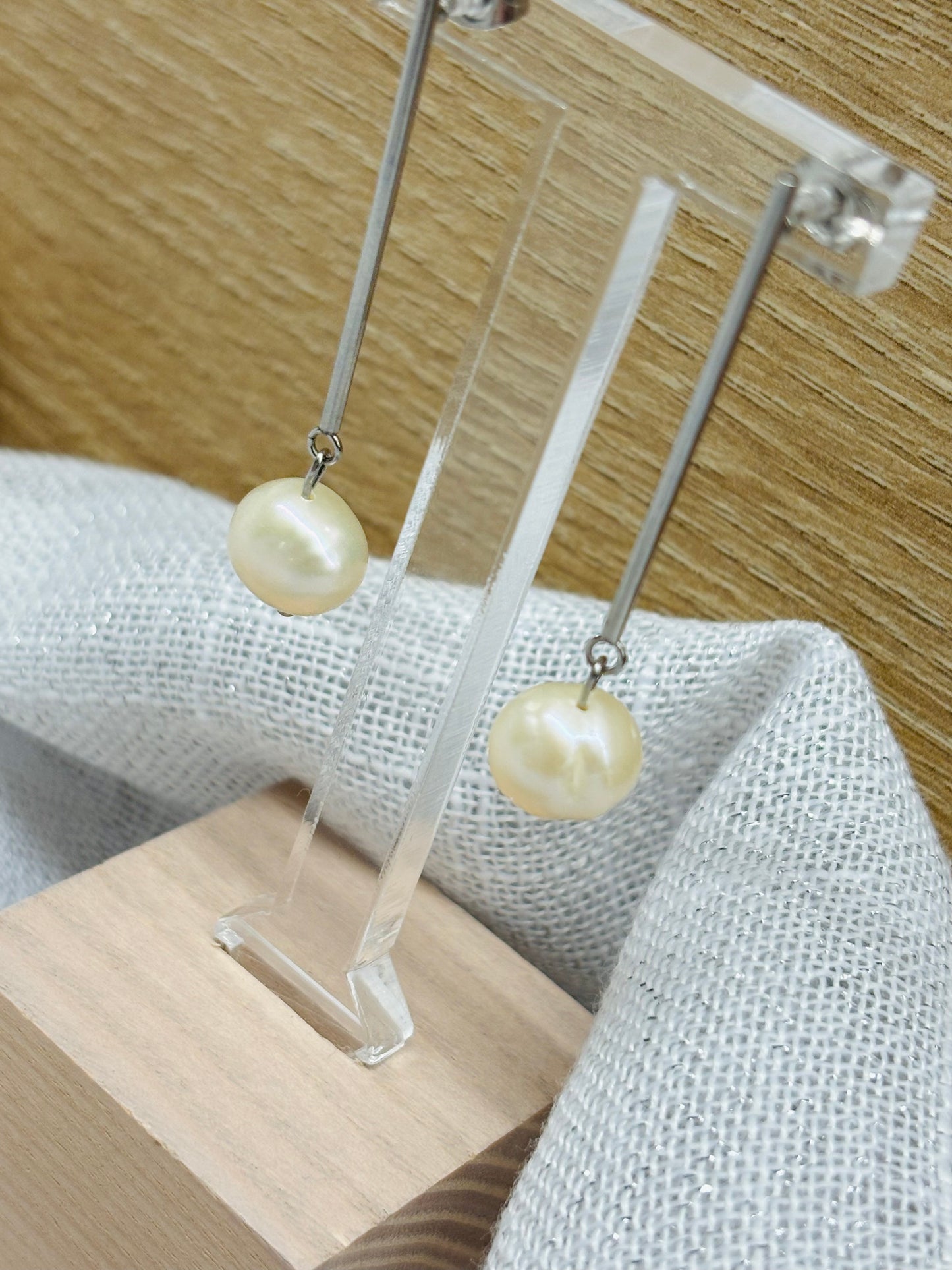 Boucles d'oreille MANON, en Perle de Culture, exposées sur un fond en bois et lin.
