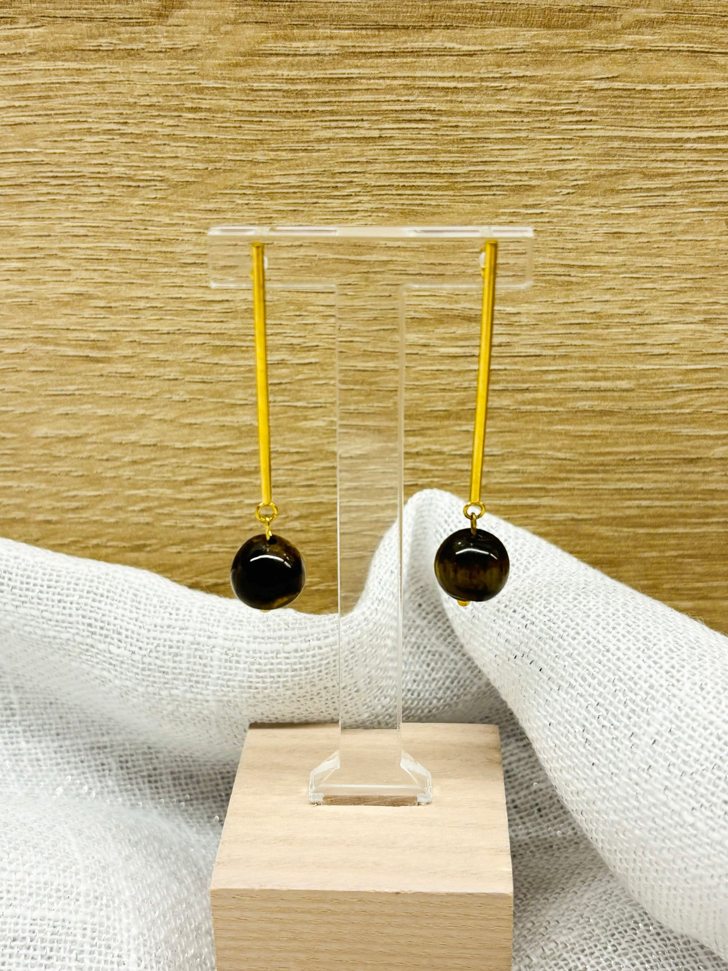 Boucles d'oreille MANON, en pierre d'Oeil de Tigre, exposées sur un fond en bois et en lin.