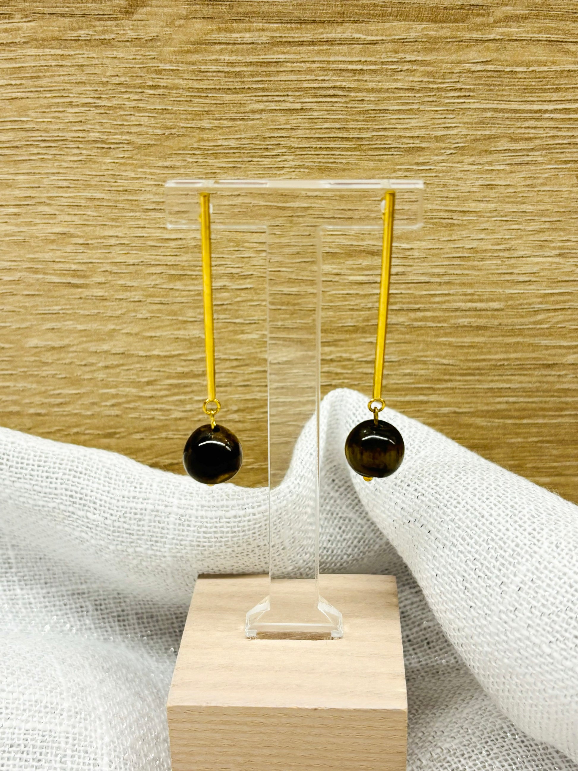 Boucles d'oreille MANON, en pierre d'Oeil de Tigre, exposées sur un fond en bois et en lin.