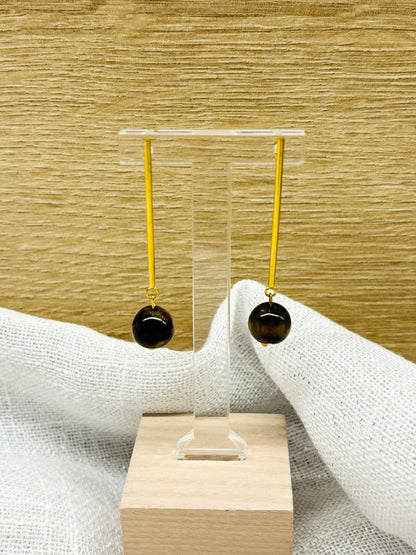 Boucles d'oreille MANON, en pierre d'Oeil de Tigre, exposées sur un fond en bois et en lin.