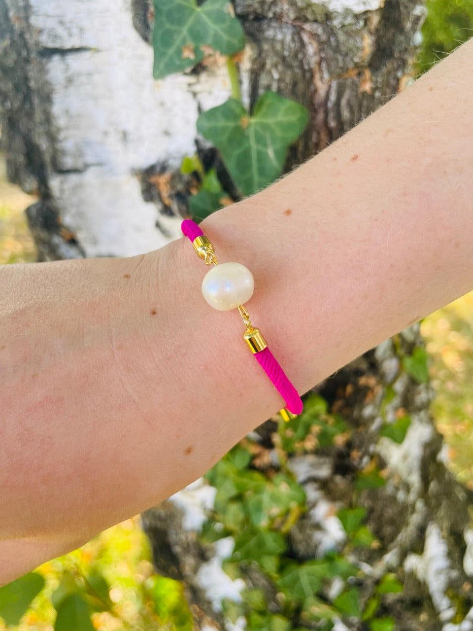 Bracelet MIA, avec cordon de couleur Fuchsia et perle de culture, porté sur un poignet de femme devant un arbre.