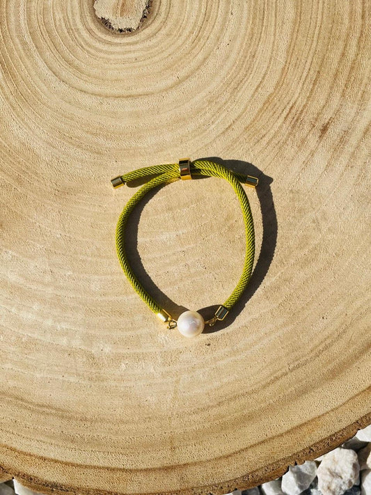Bracelet MIA, avec cordon de couleur pistache et perle de culture, exposé sur un fond en bois.