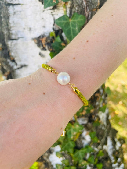 Bracelet MIA, avec cordon de couleur pistache et perle de culture, porté sur un poignet de femme devant un arbre.