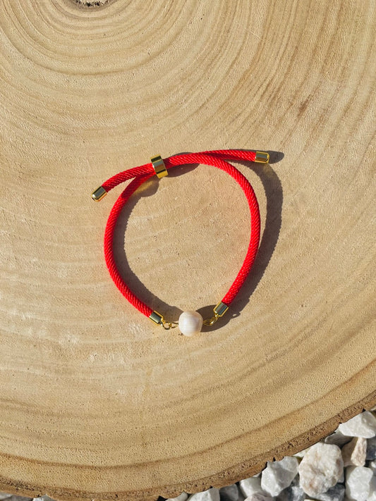 Bracelet MIA, avec cordon de couleur rouge et perle de culture, exposé sur un fond en bois.