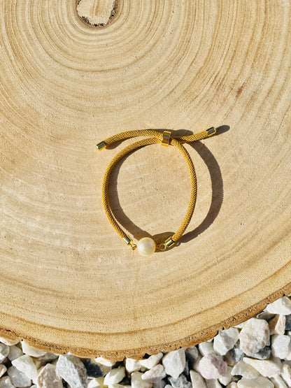 Bracelet MIA, avec cordon de couleur sable et perle de culture, exposé sur un fond en bois.