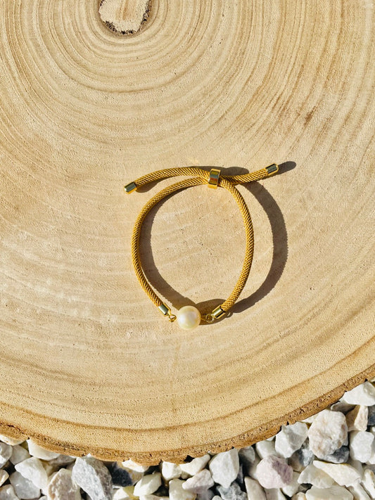 Bracelet MIA, avec cordon de couleur sable et perle de culture, exposé sur un fond en bois.