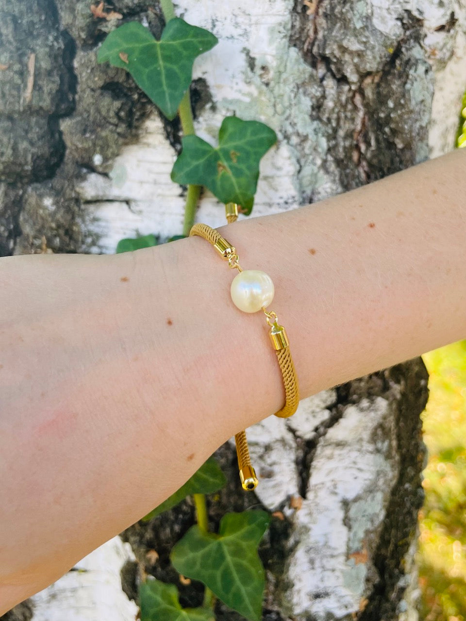 Bracelet MIA, avec cordon de couleur sable et perle de culture, porté par un poignet de femme devant un arbre.