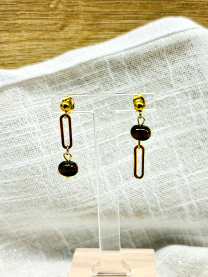 Boucles d'oreille NOËLA, avec pierre d'Oeil de Tigre, exposées sur un fond en lin.