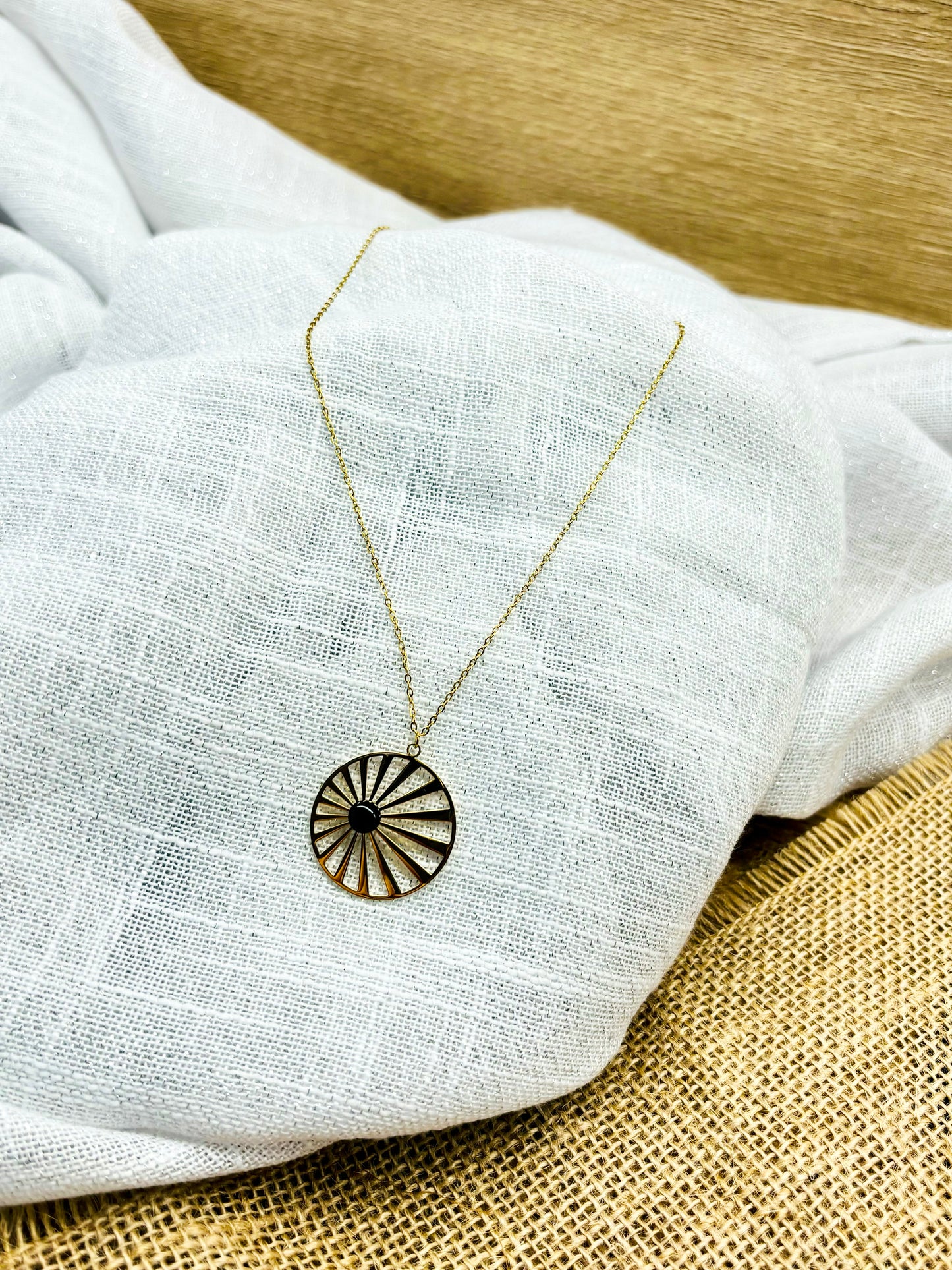 Collier SANA, de couleur dorée avec pierre d'Agate, exposé sur un fond en lin.
