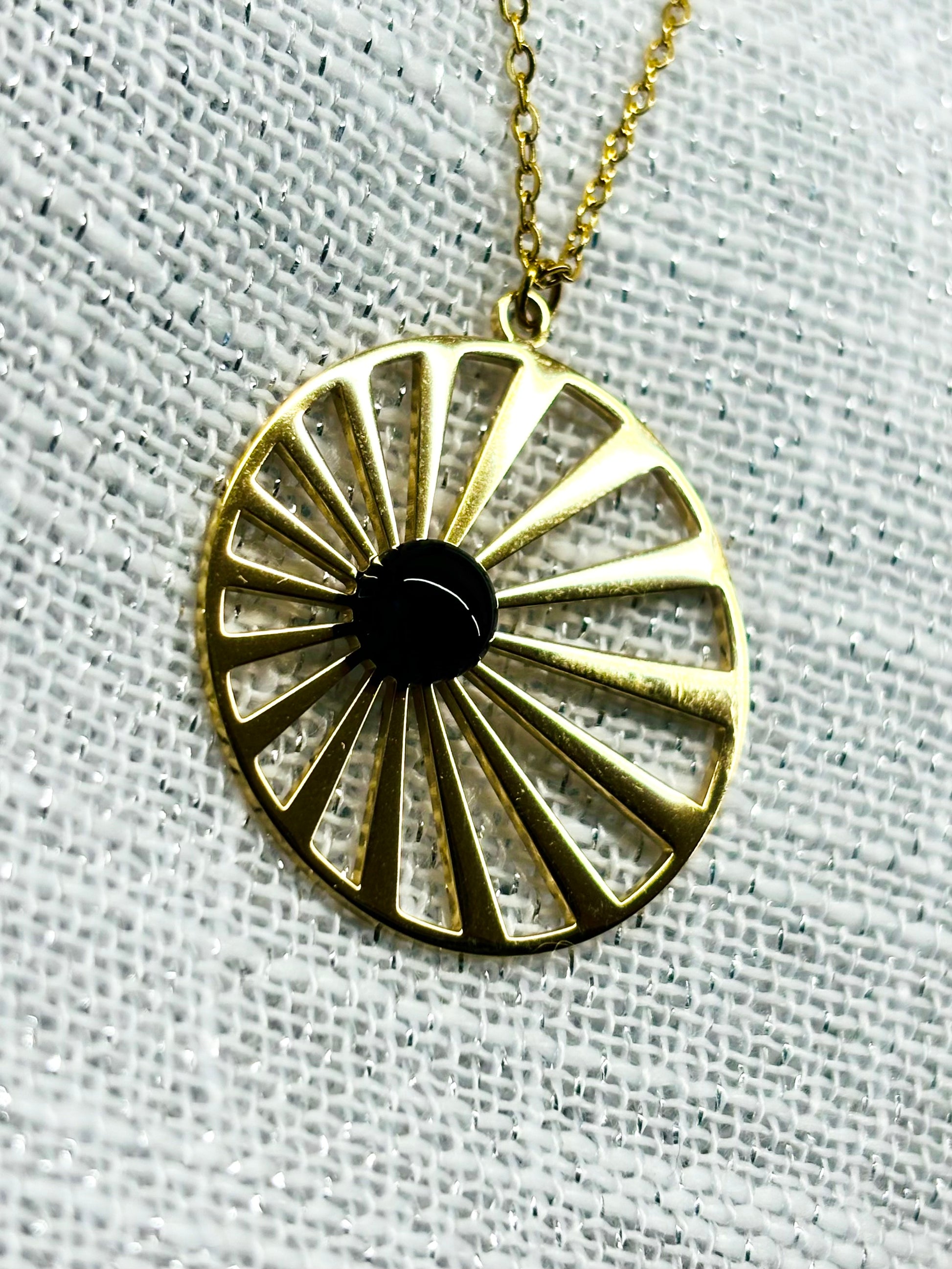 Collier SANA, de couleur dorée avec pierre d'Agate, exposé sur un fond en lin.