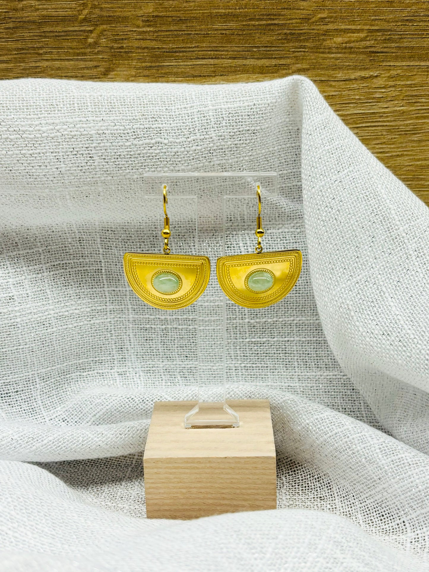 Boucles d'oreille SELENA, en acier inoxydable doré et pierre d'Aventurine, exposées sur un fond en lin.
