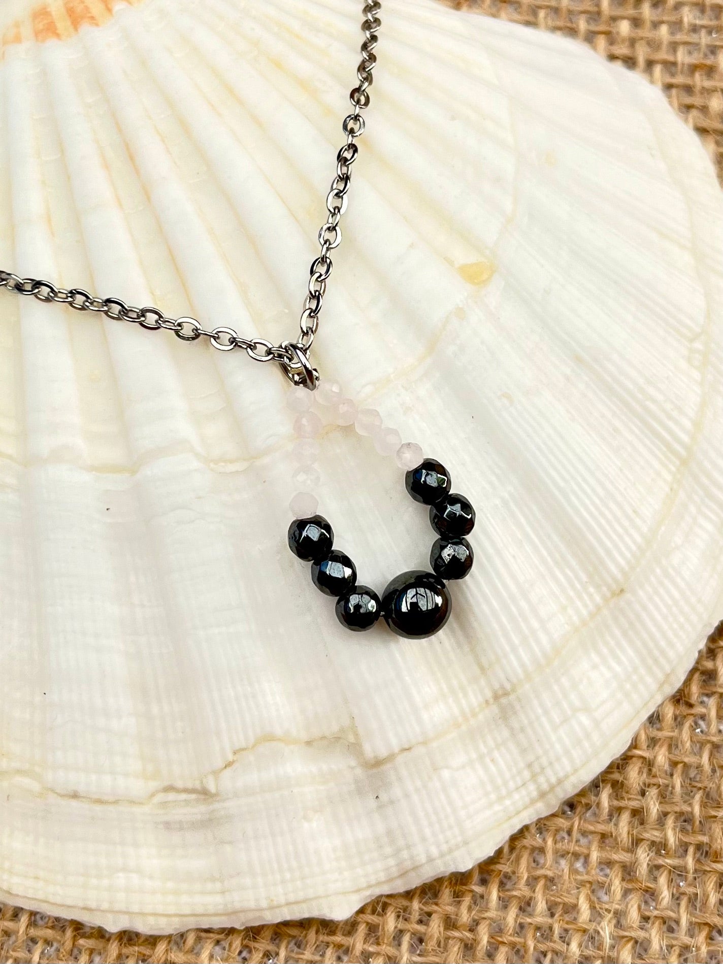 Collier SIMONA, avec pierres d'Hématites et de Quartz Rose, exposé sur un coquillage.