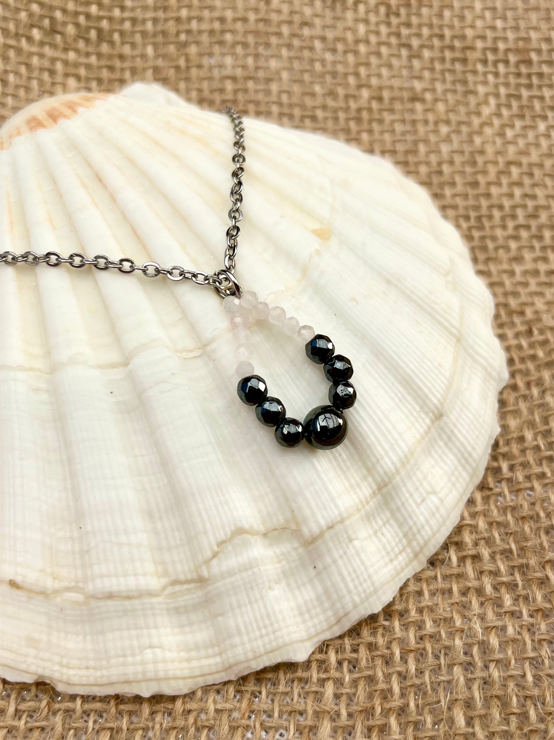 Collier SIMONA, avec pierres d'Hématites et de Quartz Rose, exposé sur un coquillage.