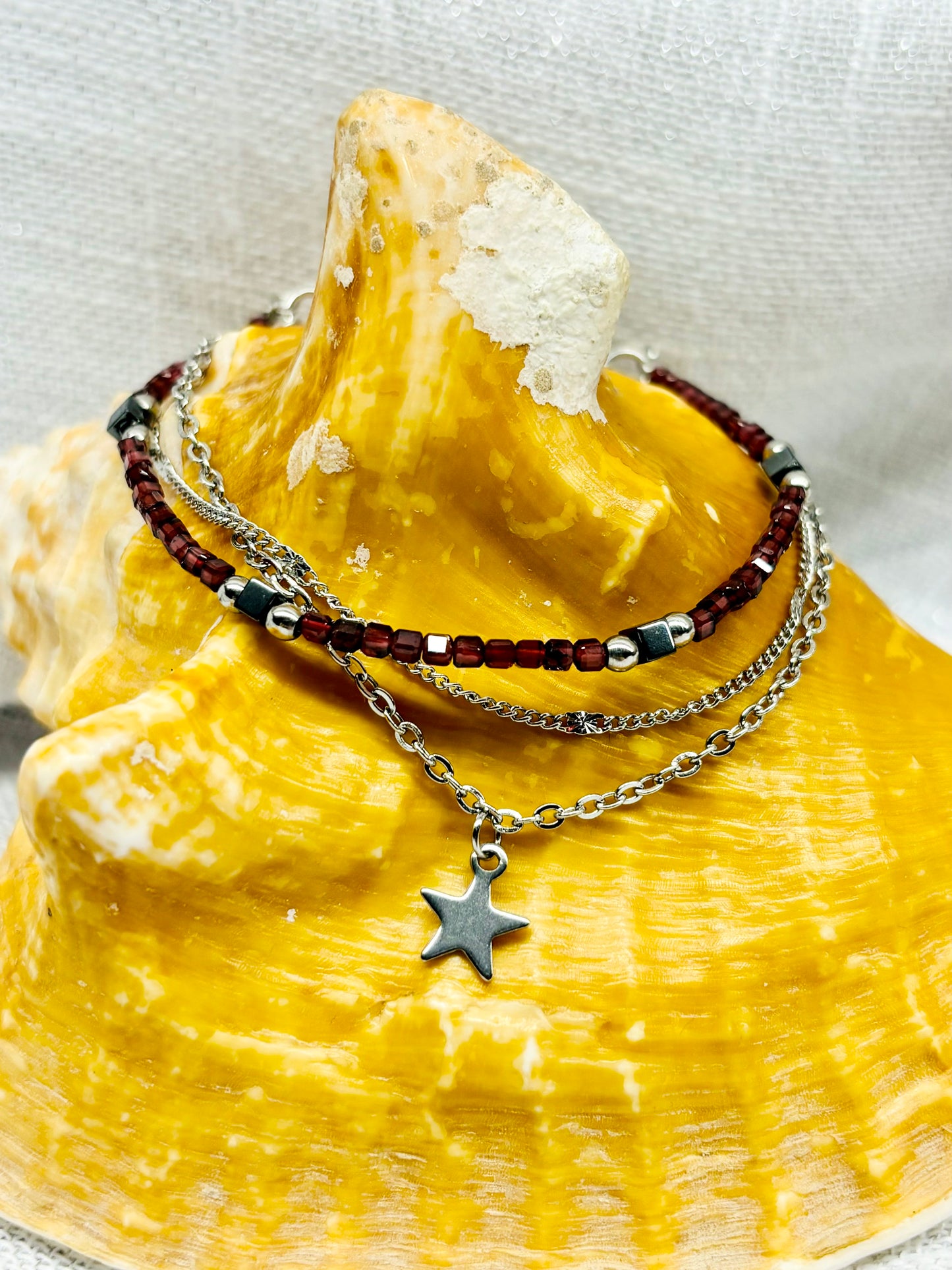 Bracelet STELLA, en acier inoxydable, avec pierre de Grenat et pierre d'Hématite, sur un coquillage.
