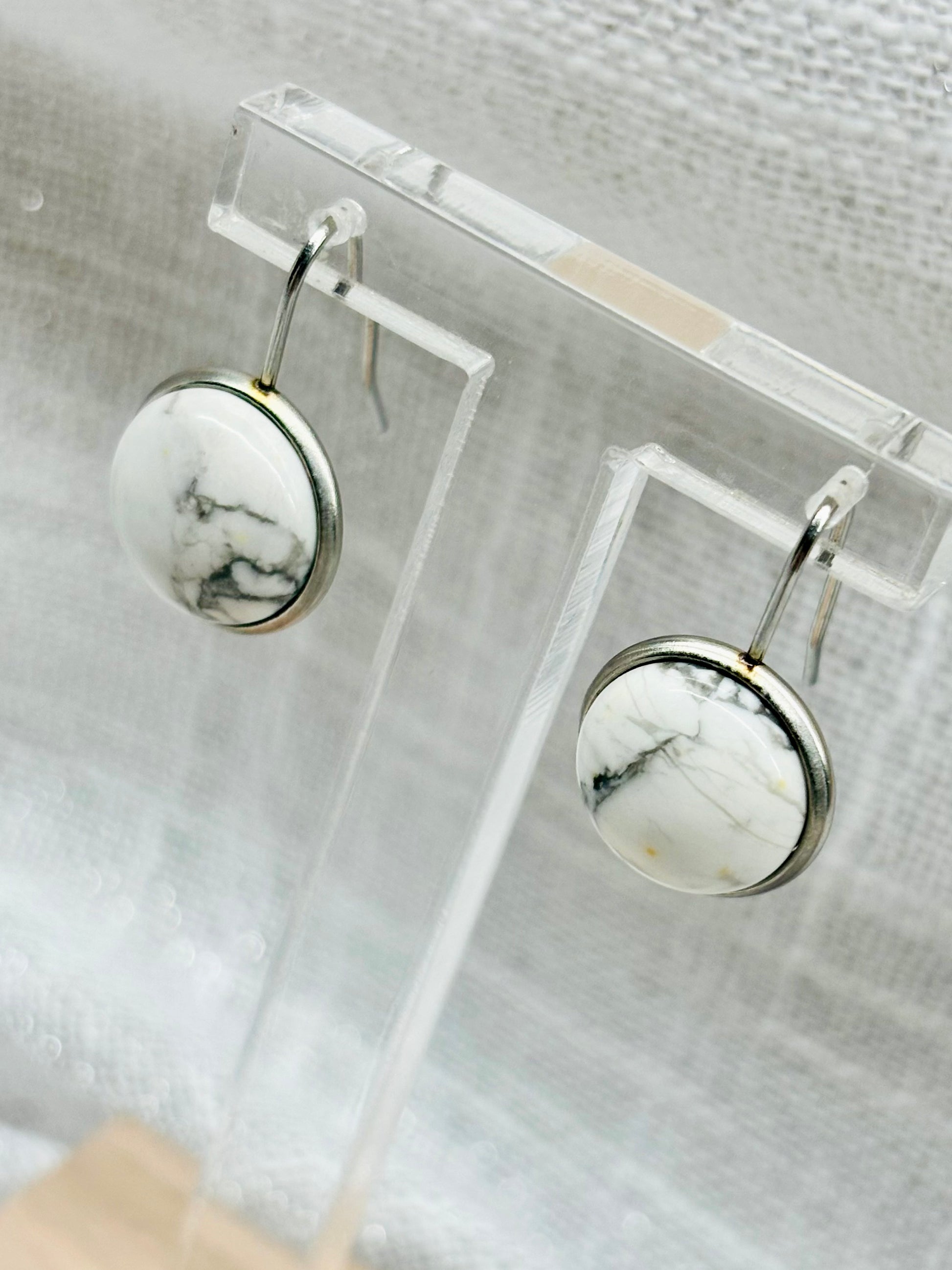 Boucles d'Oreille THÉANA, avec pierre d'howlite, exposées sur un fond en lin.