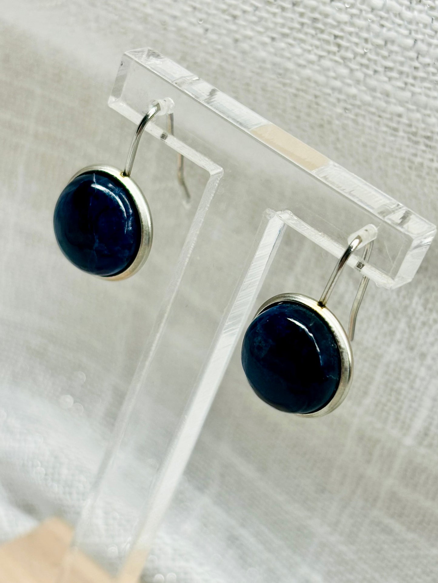 Boucles d'oreille THÉANA, avec pierre de Sodalite, exposées sur un fond en lin.