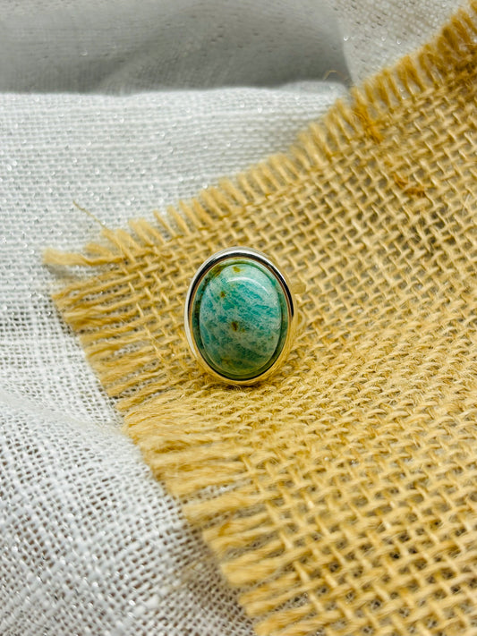 Bague THÉA, en argent et pierre d'Amazonite, exposée sur de la toile de jute et du lin.