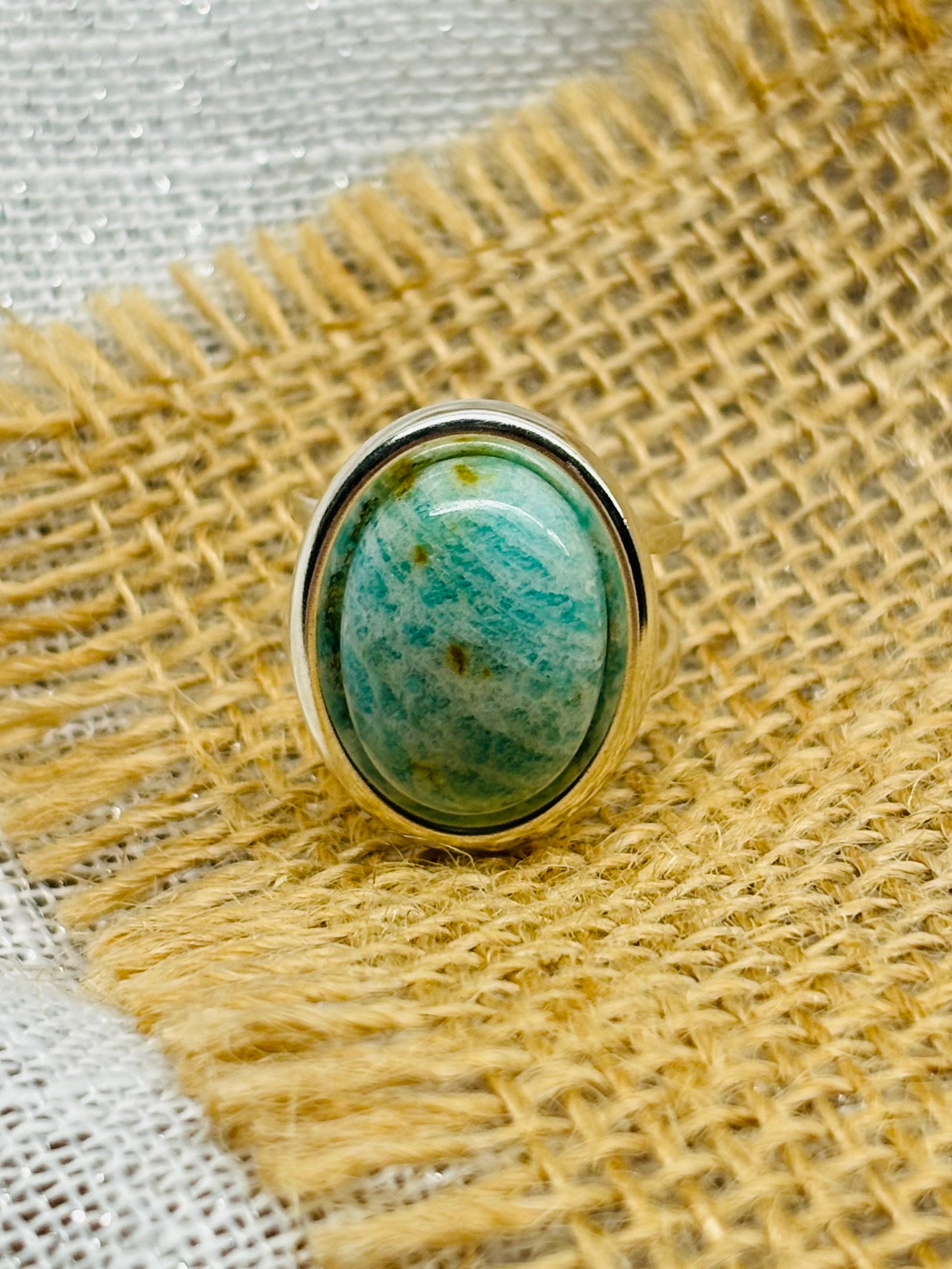 Bague THÉA, en argent et pierre d'Amazonite, exposée sur de la toile de jute et du lin.
