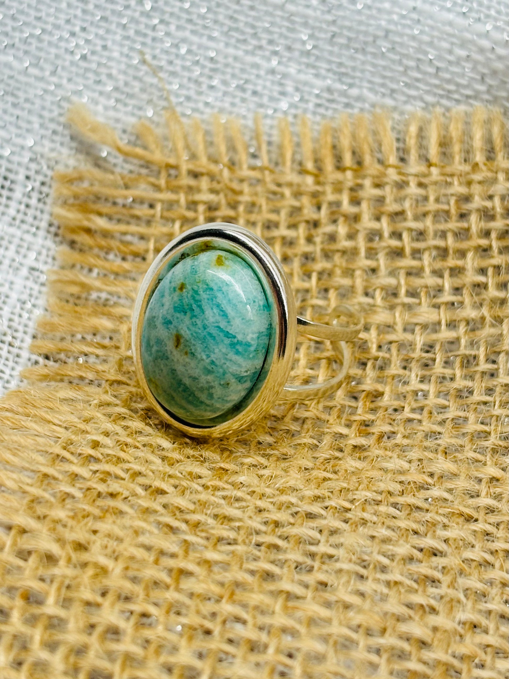 Bague THÉA, en argent et pierre d'Amazonite, exposée sur de la toile de jute et du lin.