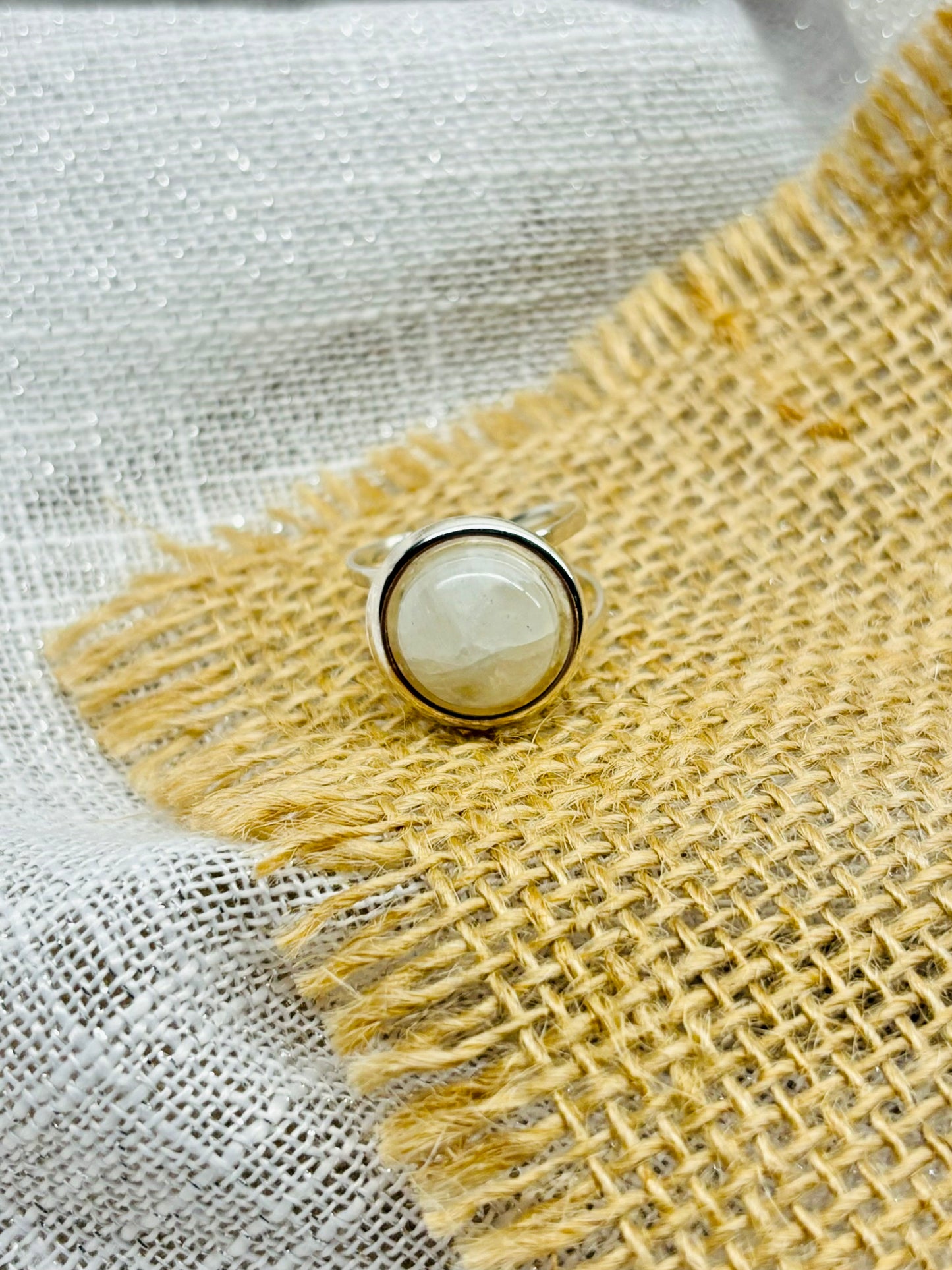 Bague THÉA, en argent et pierre de Lune, sur un fond en lin et toile de jute.