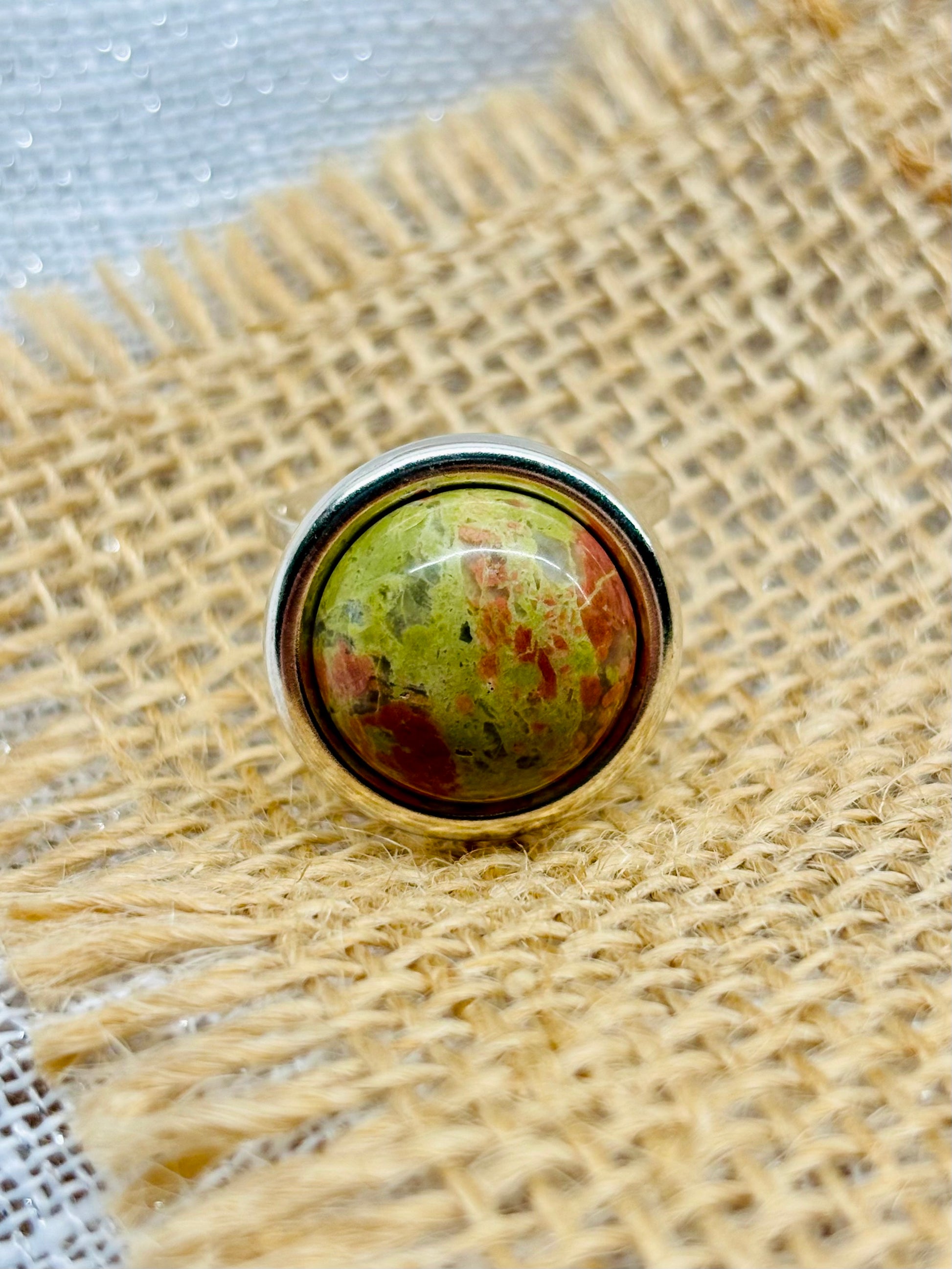 Bague THÉA, en argent et pierre d'Unakite, sur un fond en lin et toile de jute.