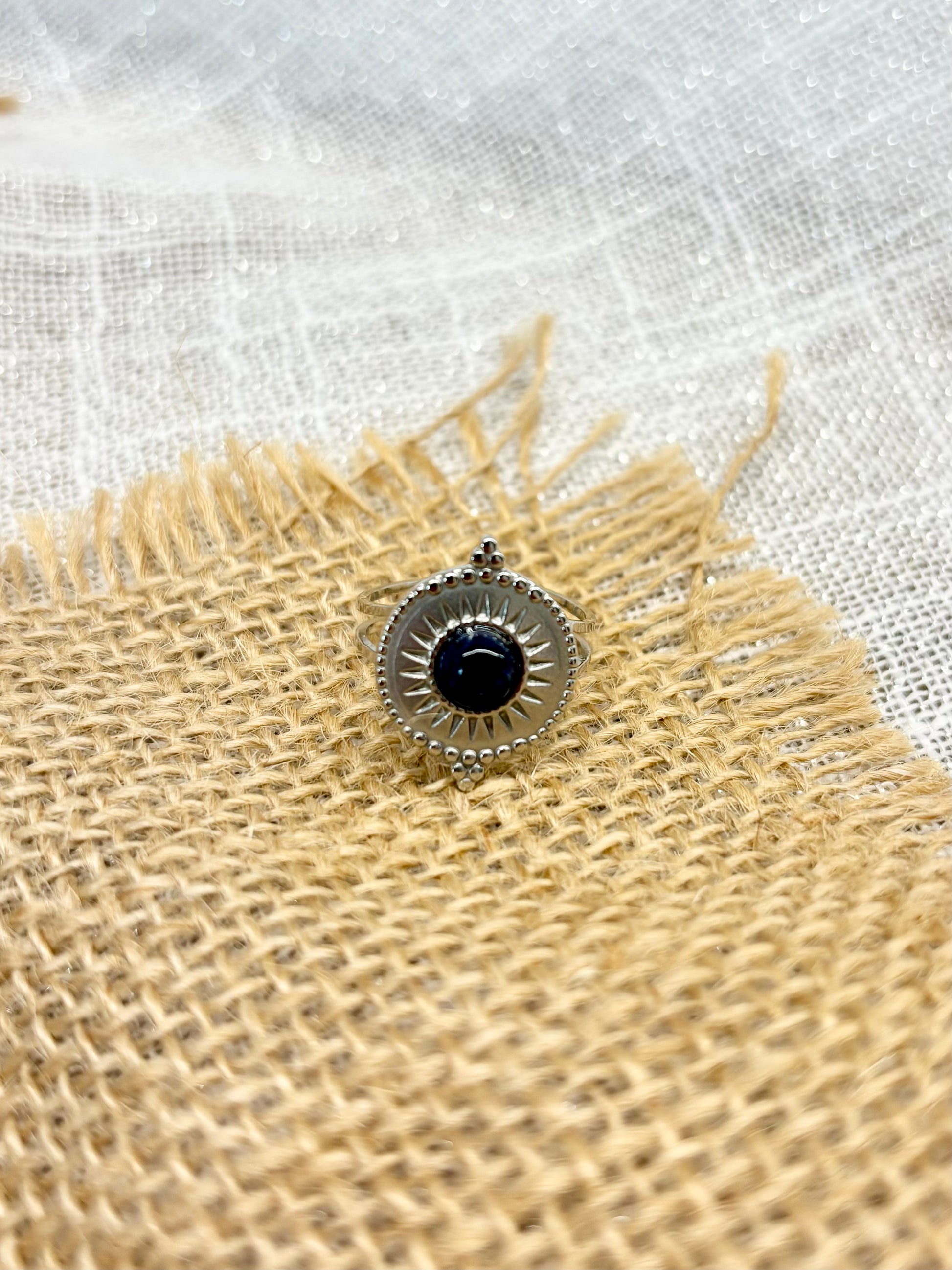 Bague ZÉLIE en acier inoxydable argent et pierre de Sodalite, exposé sur de la toile de jute et un fond en lin.