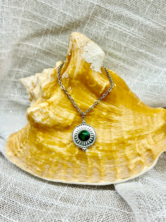 Collier ZÉLIE en acier inoxydable argent et pierre de Malachite, exposé sur un coquillage et un fond en lin