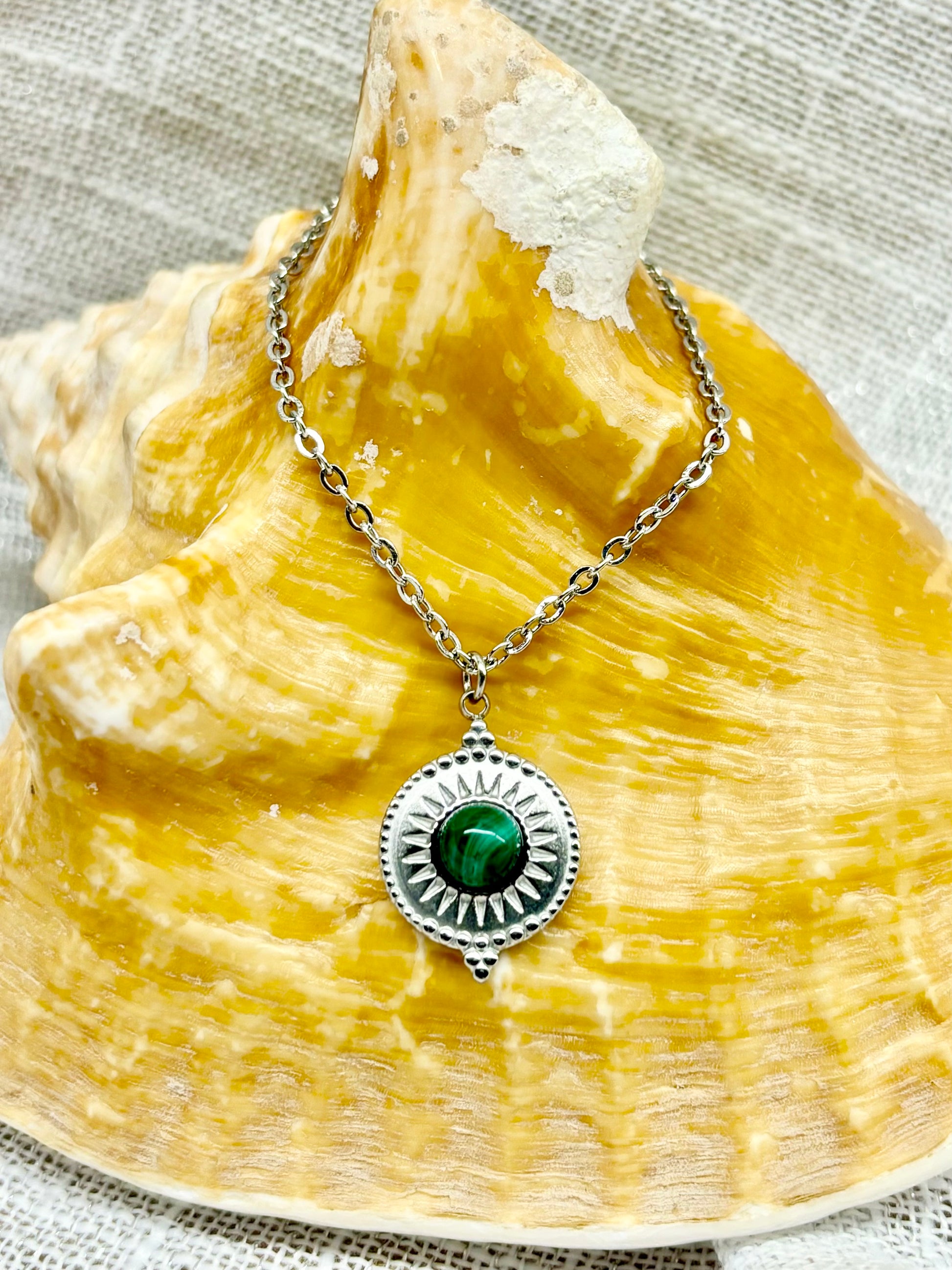 Collier ZÉLIE en acier inoxydable argent et pierre de Malachite, exposé sur un coquillage et un fond en lin