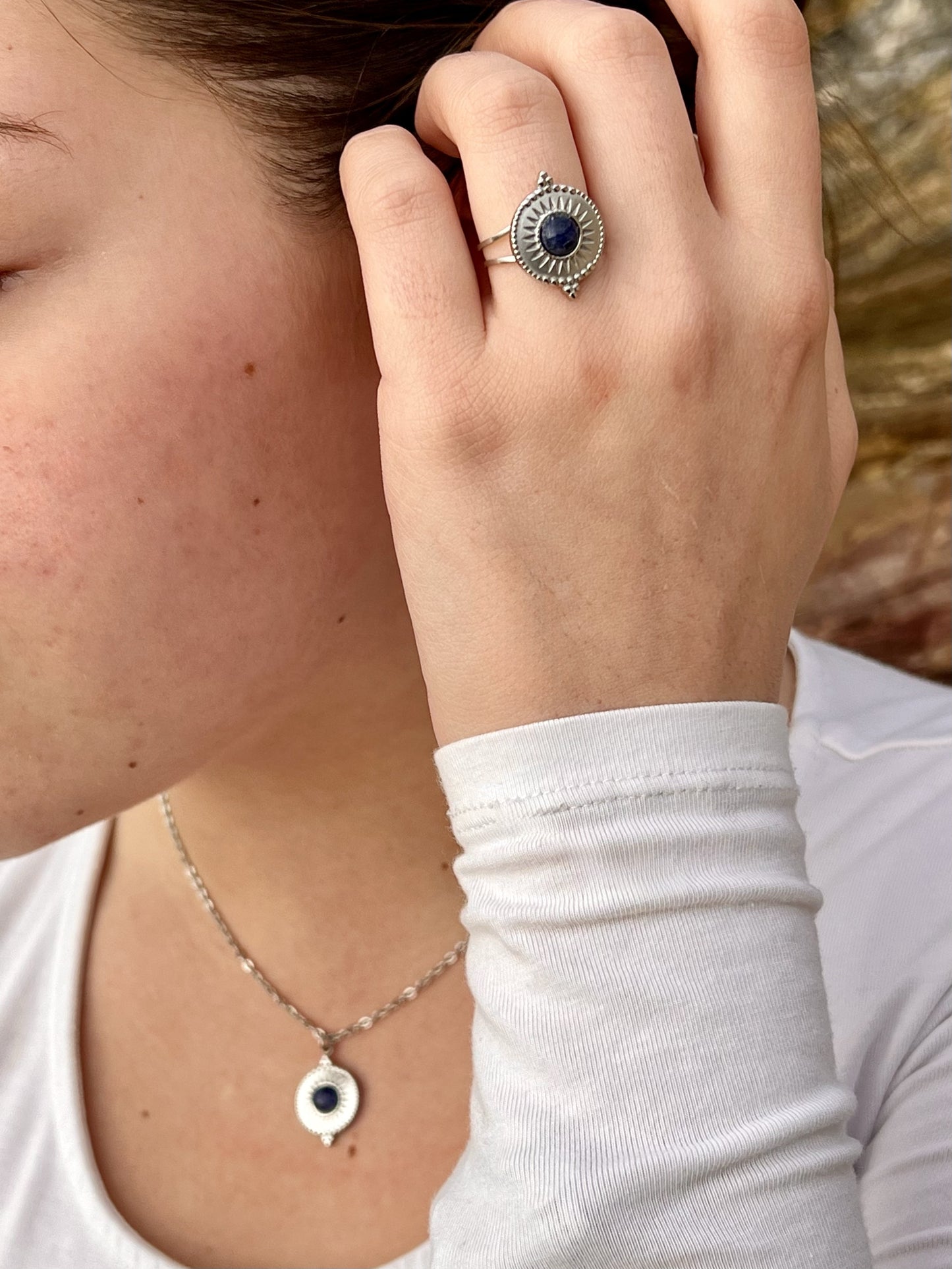 Collier et bague ZÉLIE en acier inoxydable argent avec une pierre de Sodalite, porté par une fille dans les rochers.