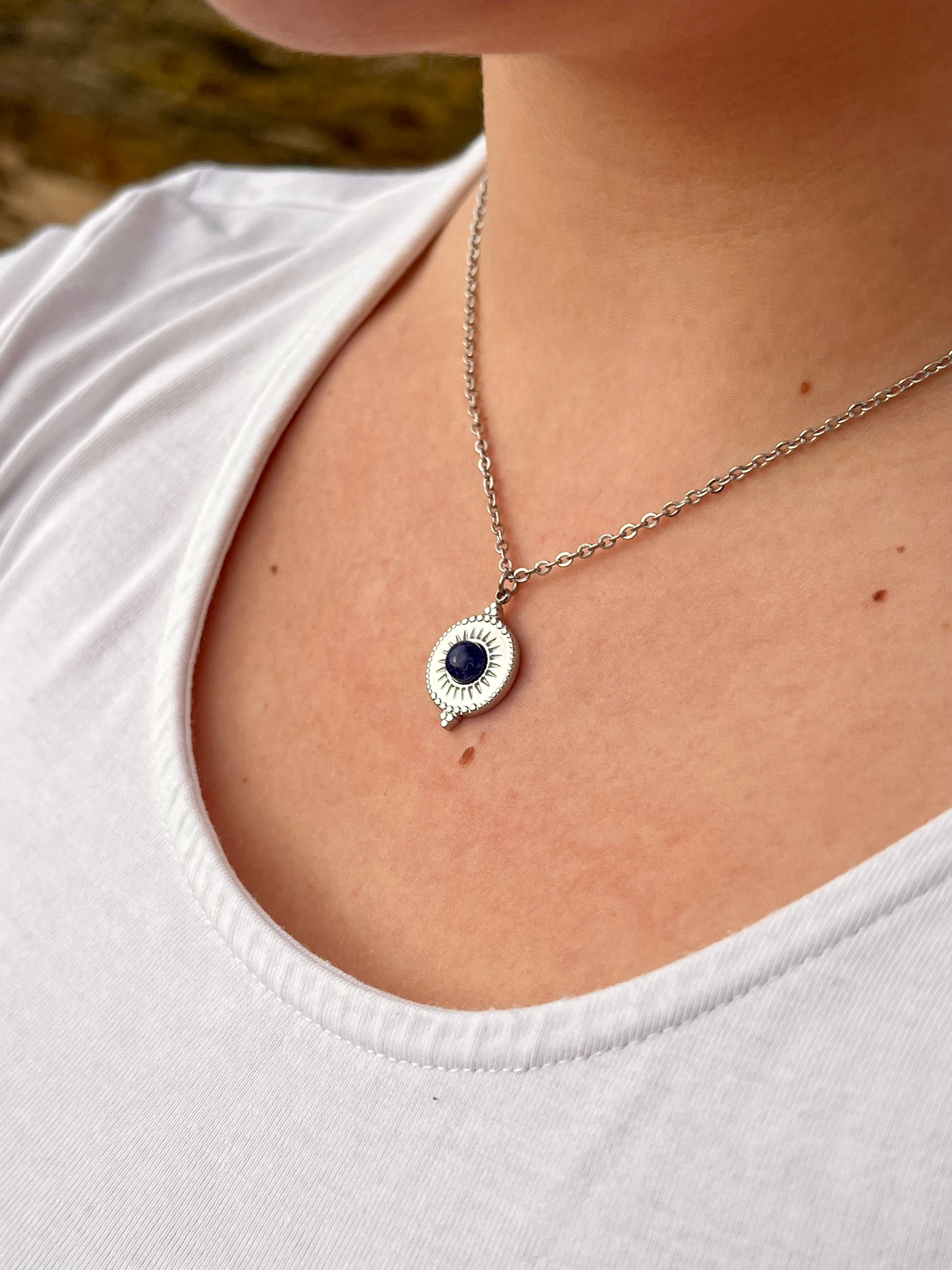 Collier ZÉLIE en acier inoxydable argent avec une pierre de Sodalite, porté par une fille dans les rochers.
