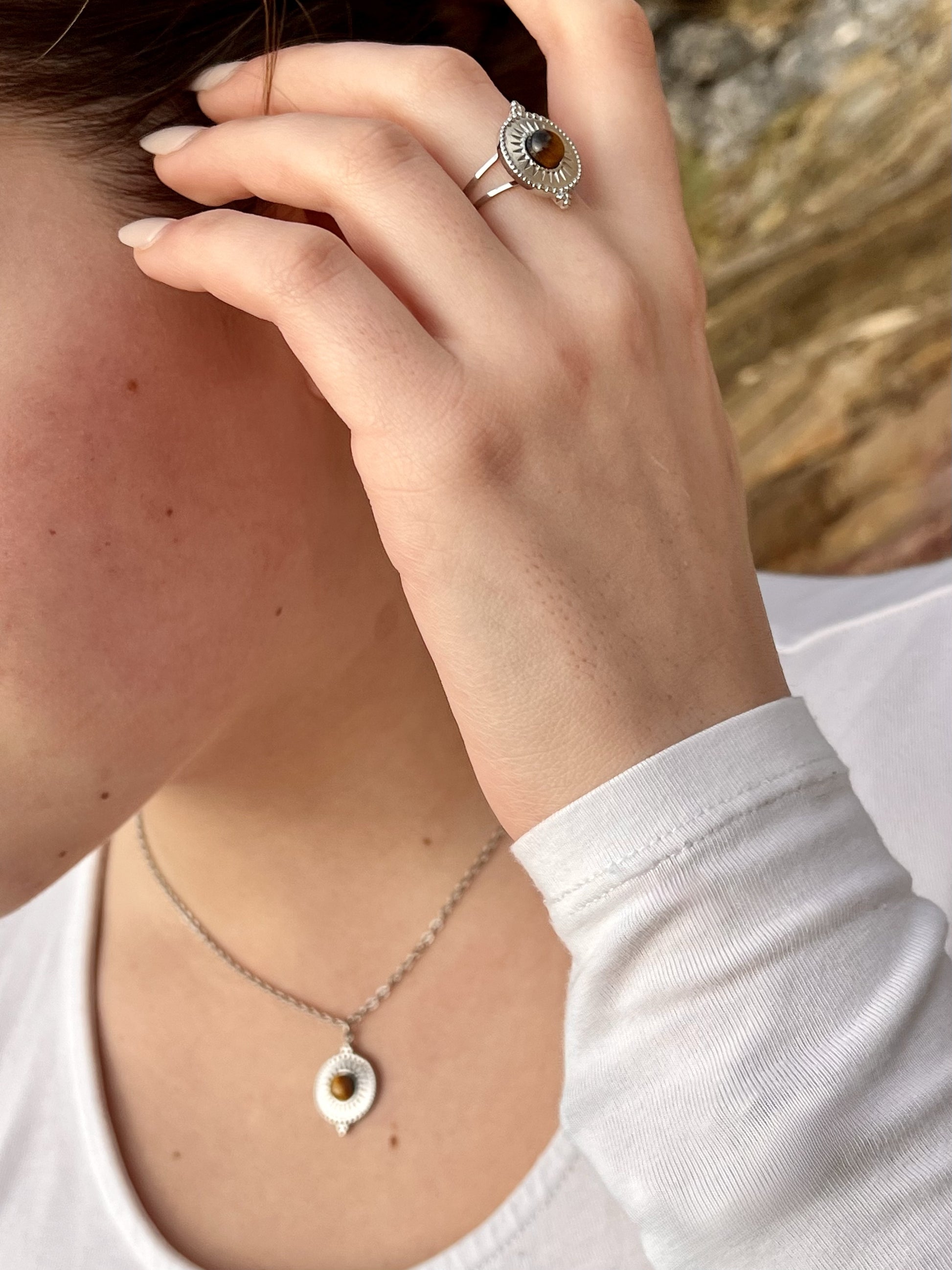 Collier et Bague ZÉLIE en acier inoxydable argent et pierre d'oeil de tigre, porté par une fille dans les rochers